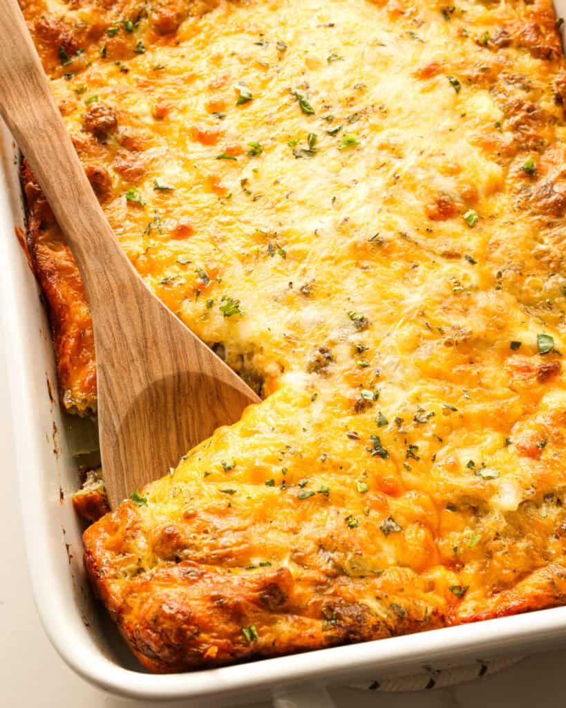 A casserole and a wooden spoon full of crescent roll breakfast casserole. 