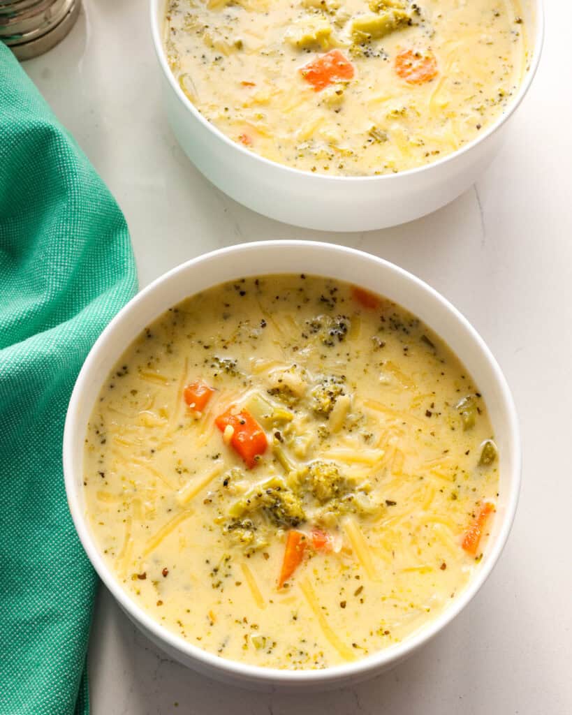 Two single serving bowls full of crockpot broccoli cheddar soup. 