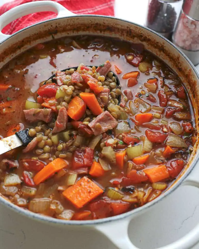 A Dutch oven and a ladle full of ham and lentil soup.