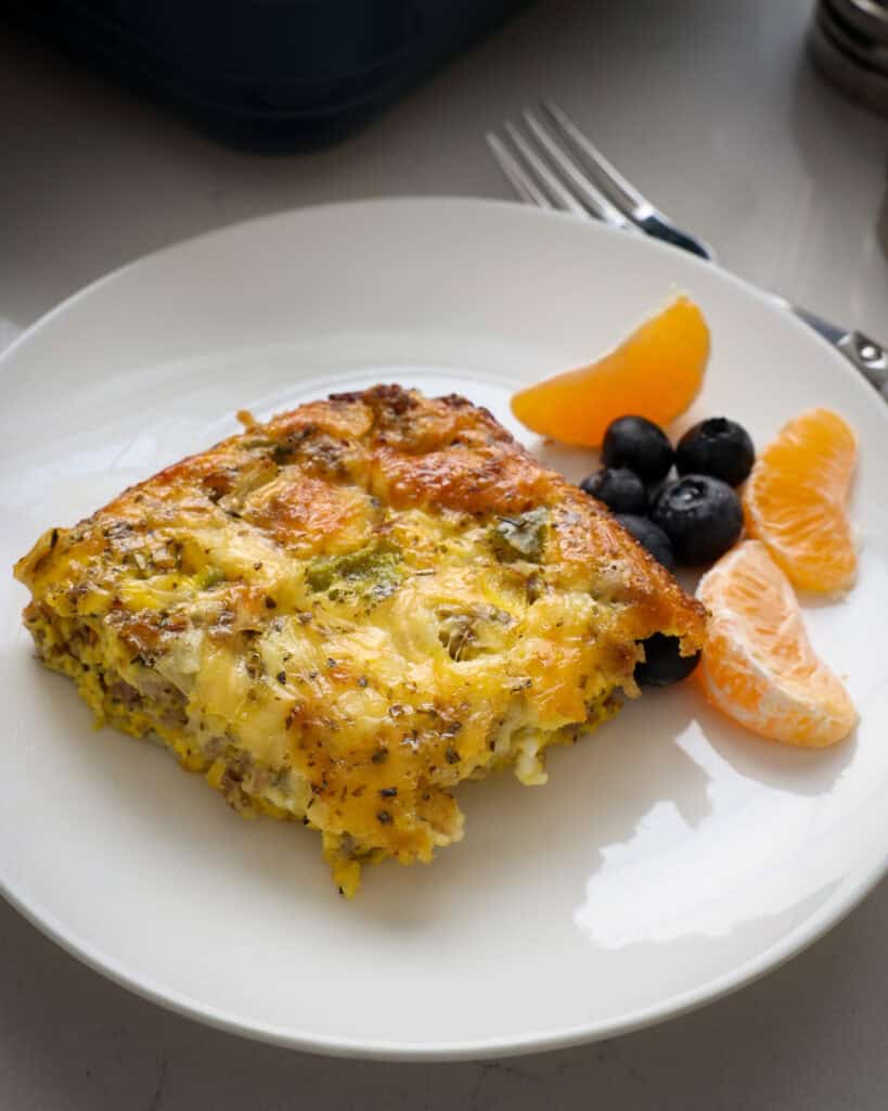 A single serving white plate with a piece of breakfast casserole and fruit salad. 