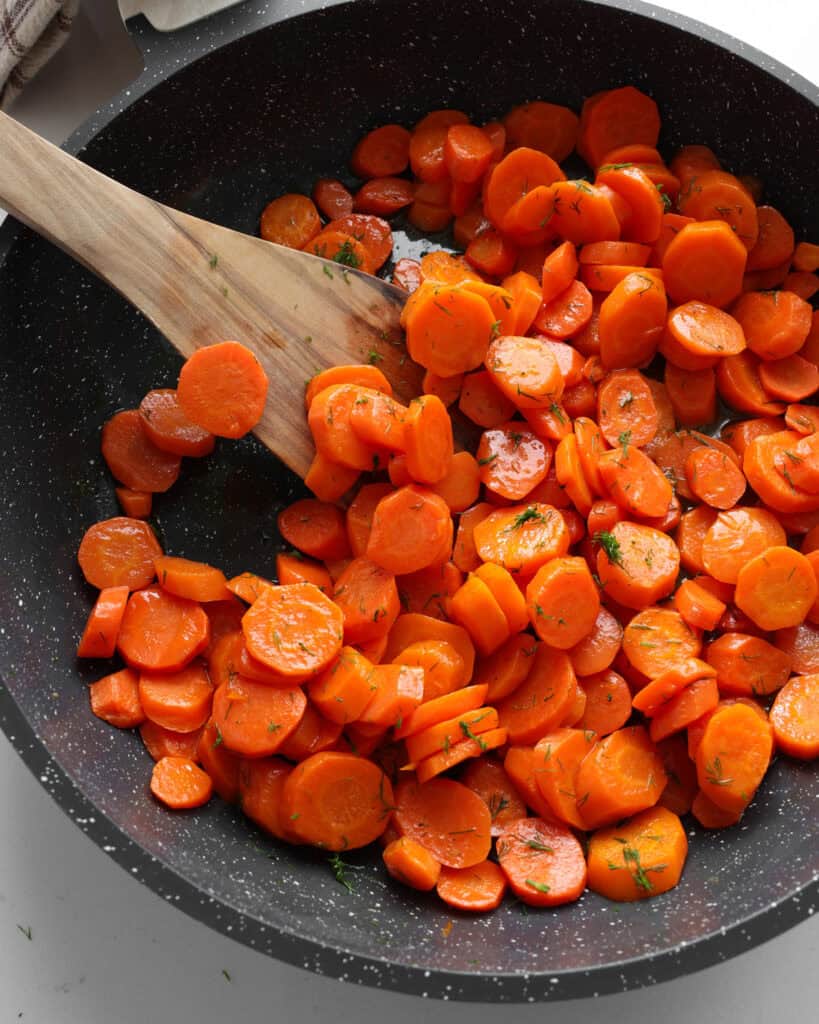A black skillet full of sauteed carrots. 