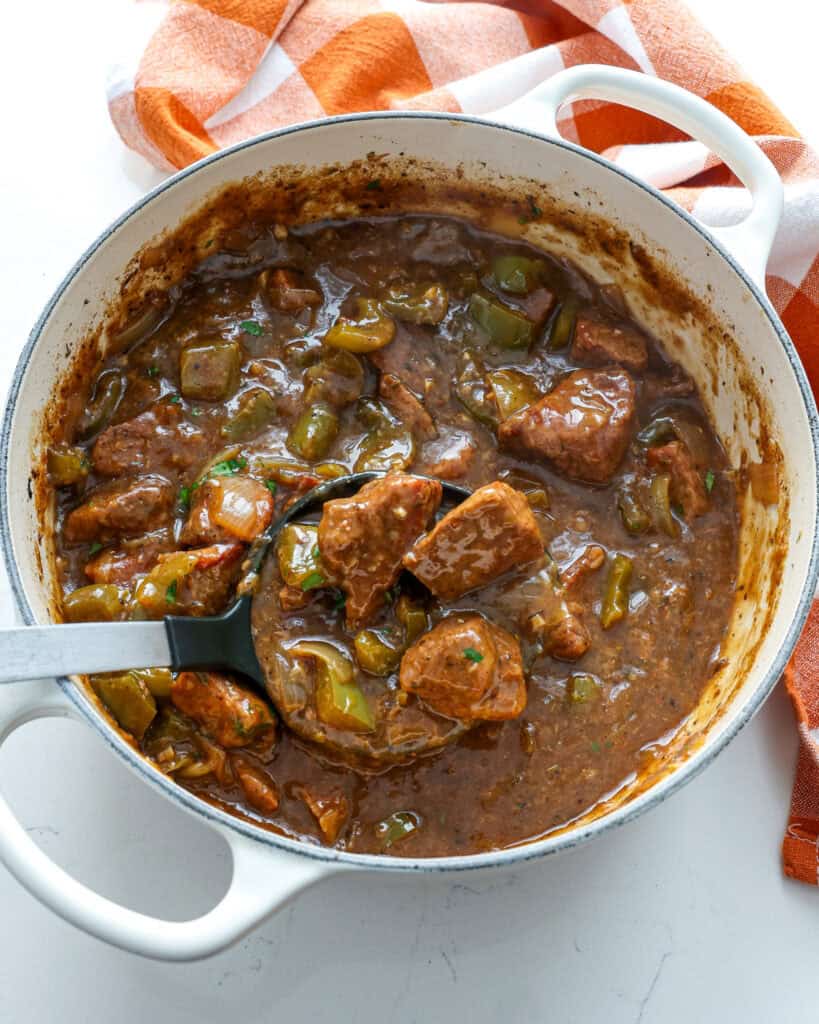 An overhead view of a Dutch oven and ladle full of beef tips and gravy. 
