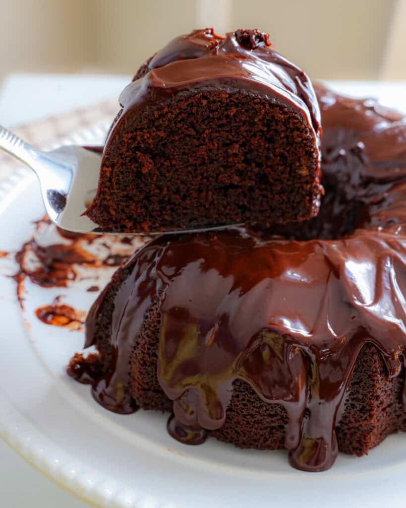 A piece of chocolate cake on a cake server over the rest of the chocolate bundt cake.
