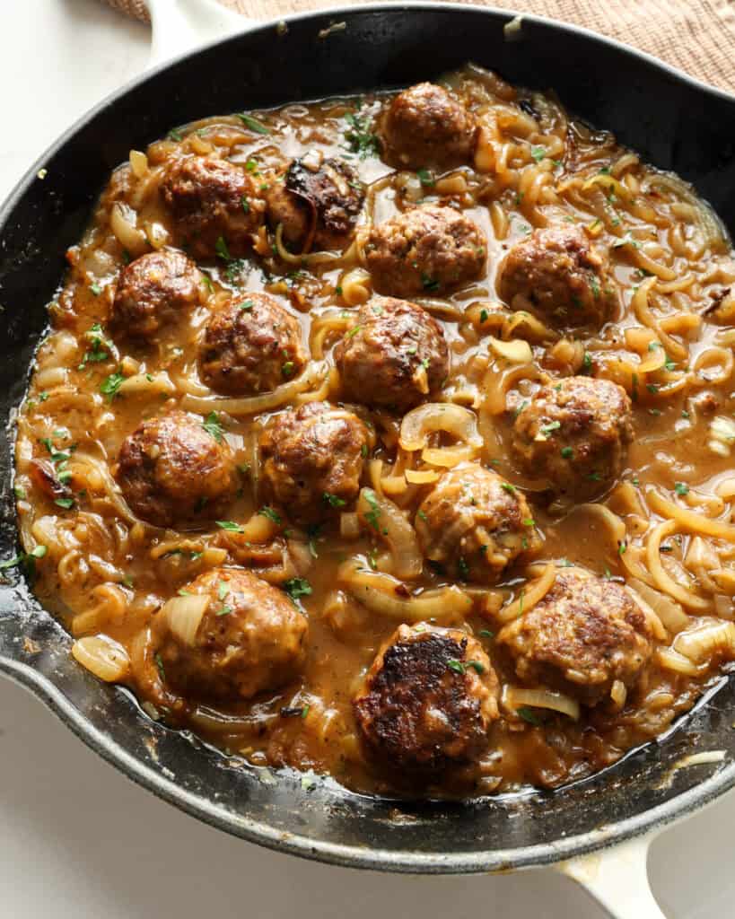 An overhead view of a white skillet full of French onion meatballs. 