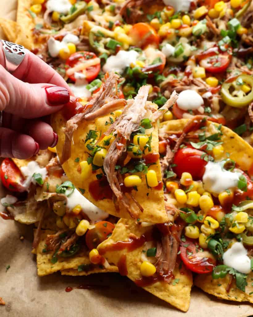 A close up view of pulled pork, cheese, corn, green onions, cilantro, and barbecue sauce on a tortilla chip. 