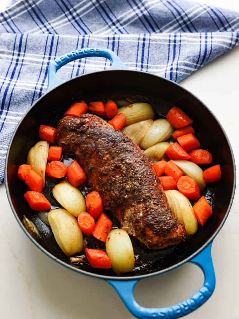 An overhead view of of a well seasoned baked pork tenderloin in a cast iron skillet with onions and carrots. 