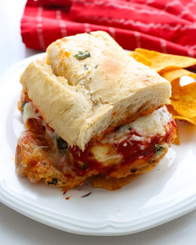 A close up view of a chicken parmesan sandwich on a plate with chips. 