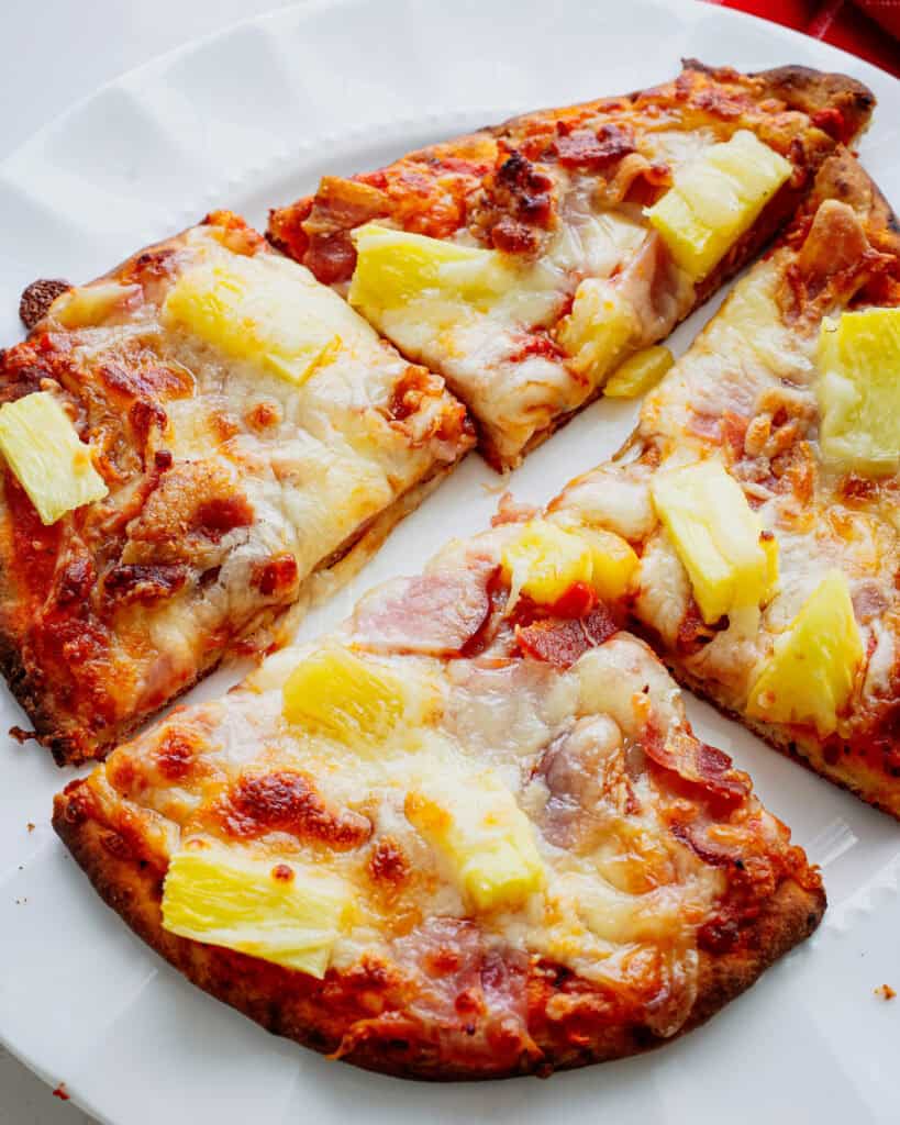 Hawaiian pizza on Naan bread on a white serving plate. 