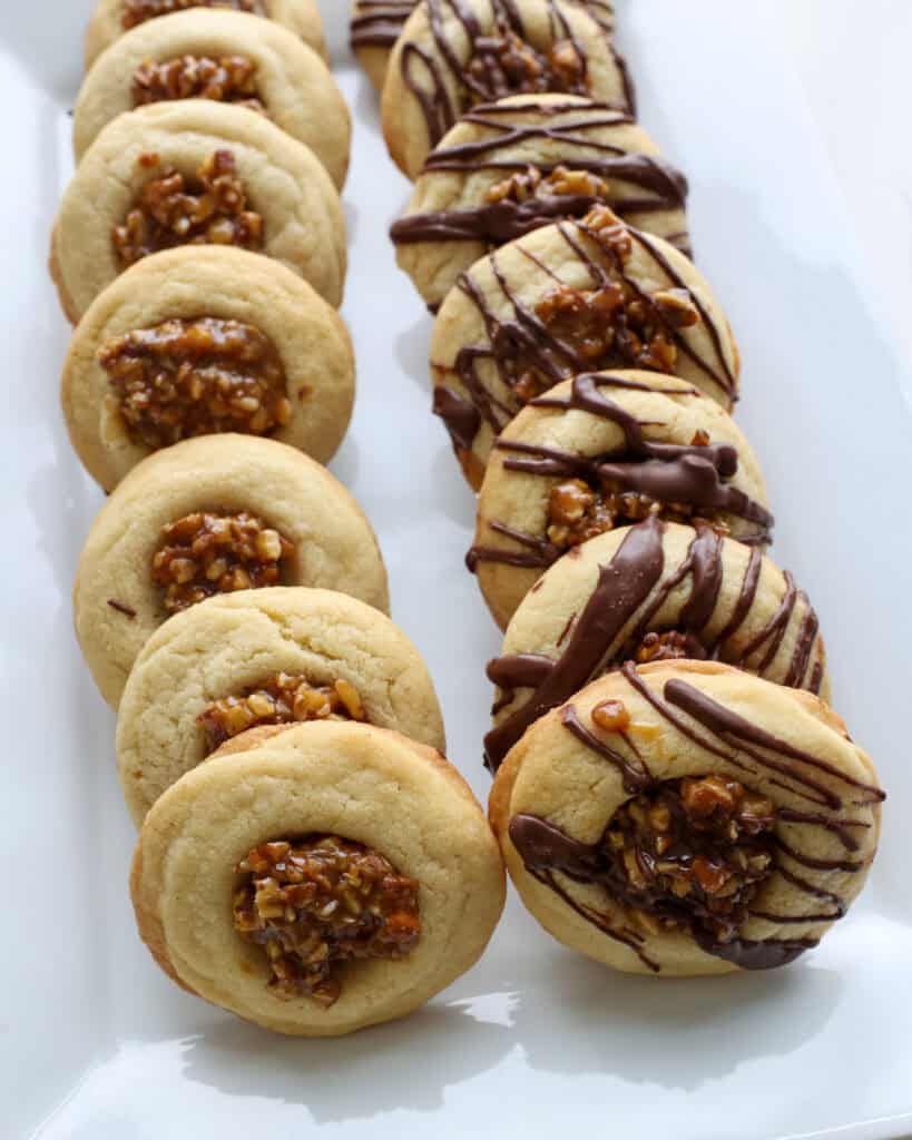 Two rows of pecan pie cookies on a rectangular white serving platter. One with drizzled chocolate and one without. 
