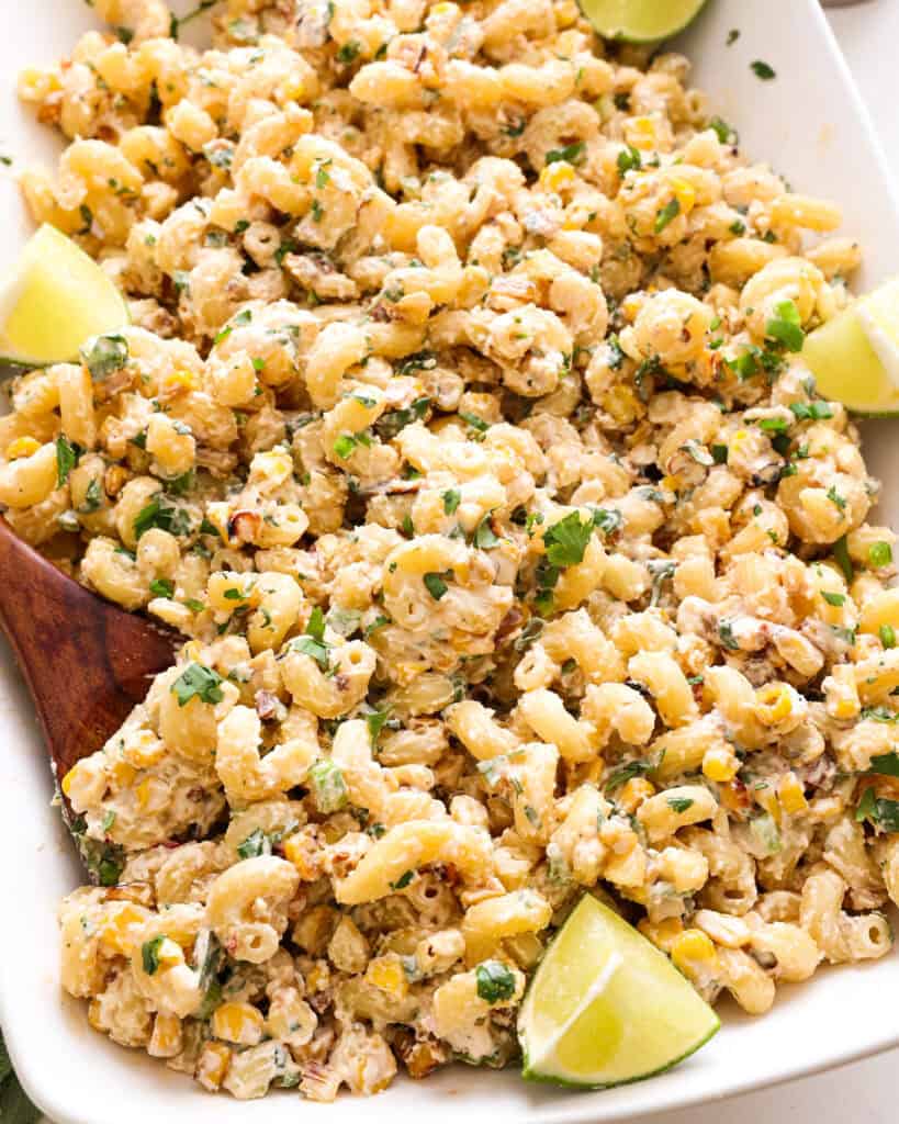 A close up view of stree corn pasta salad in a white serving bowl with lime wedges. 