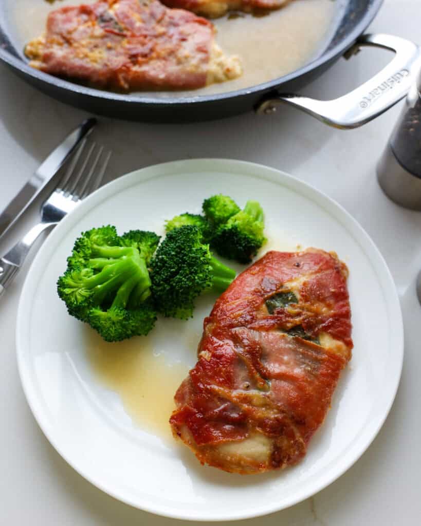 A white serving plate with chicken saltimbocca and steamed broccoli. 