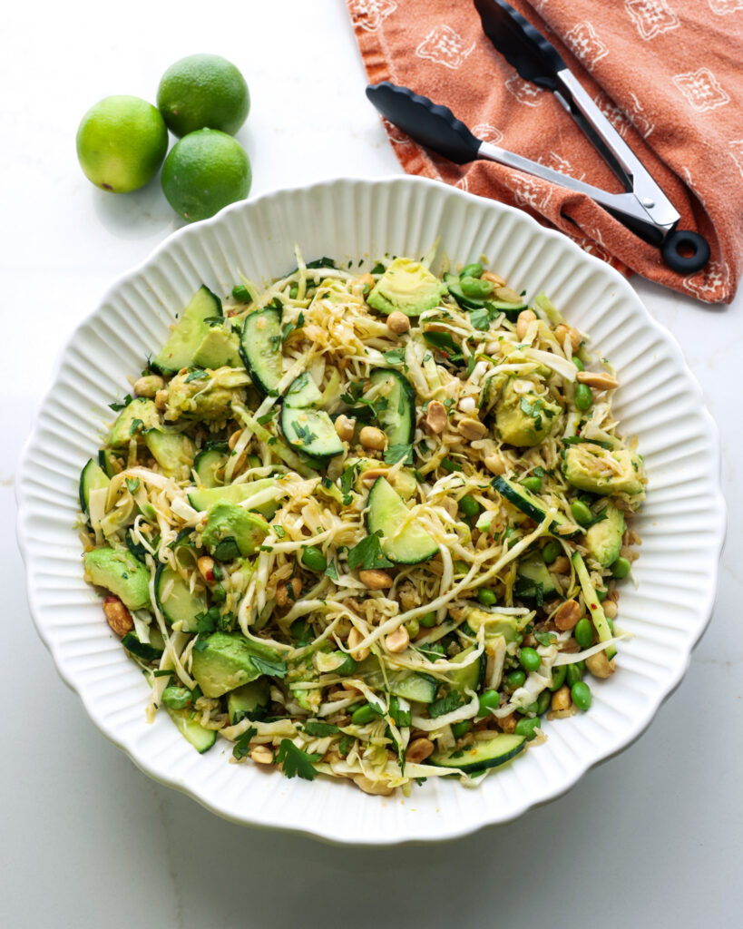 Crispy rice salad in a bowl with a pair of tongs, orange towel, and limes. 