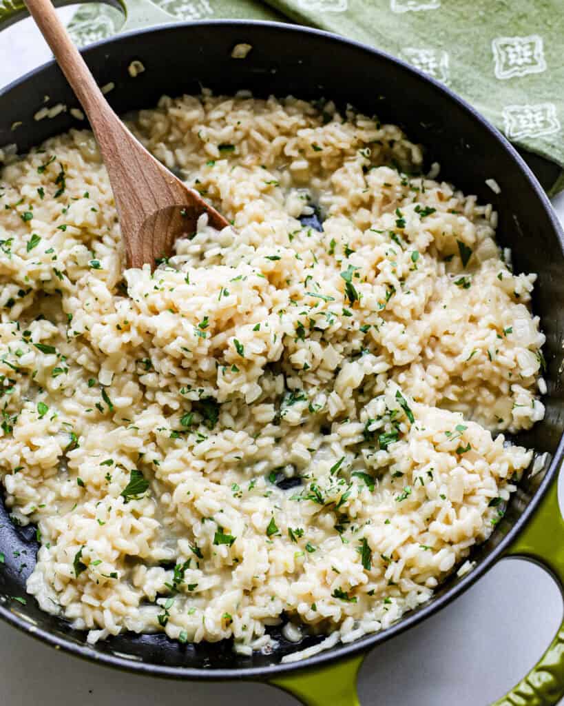 A wooden spoon and skilltet full of Parmesan risotto.