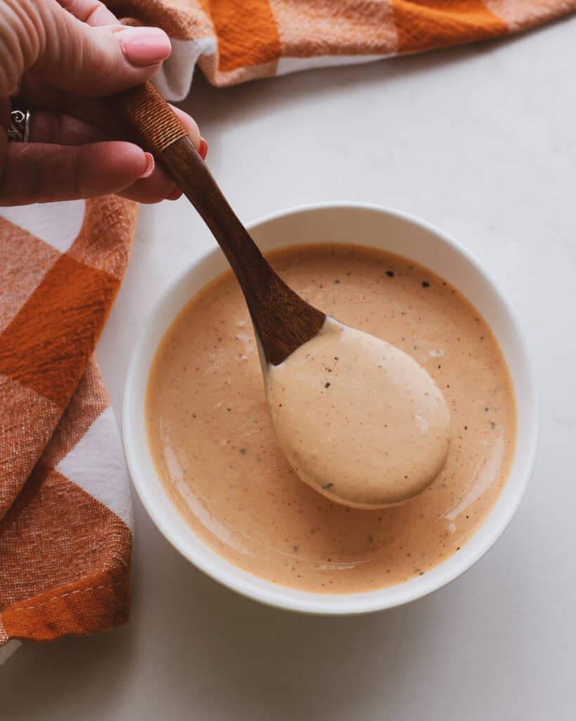 A bowl and a wooden spoon full of cane's sauce. 