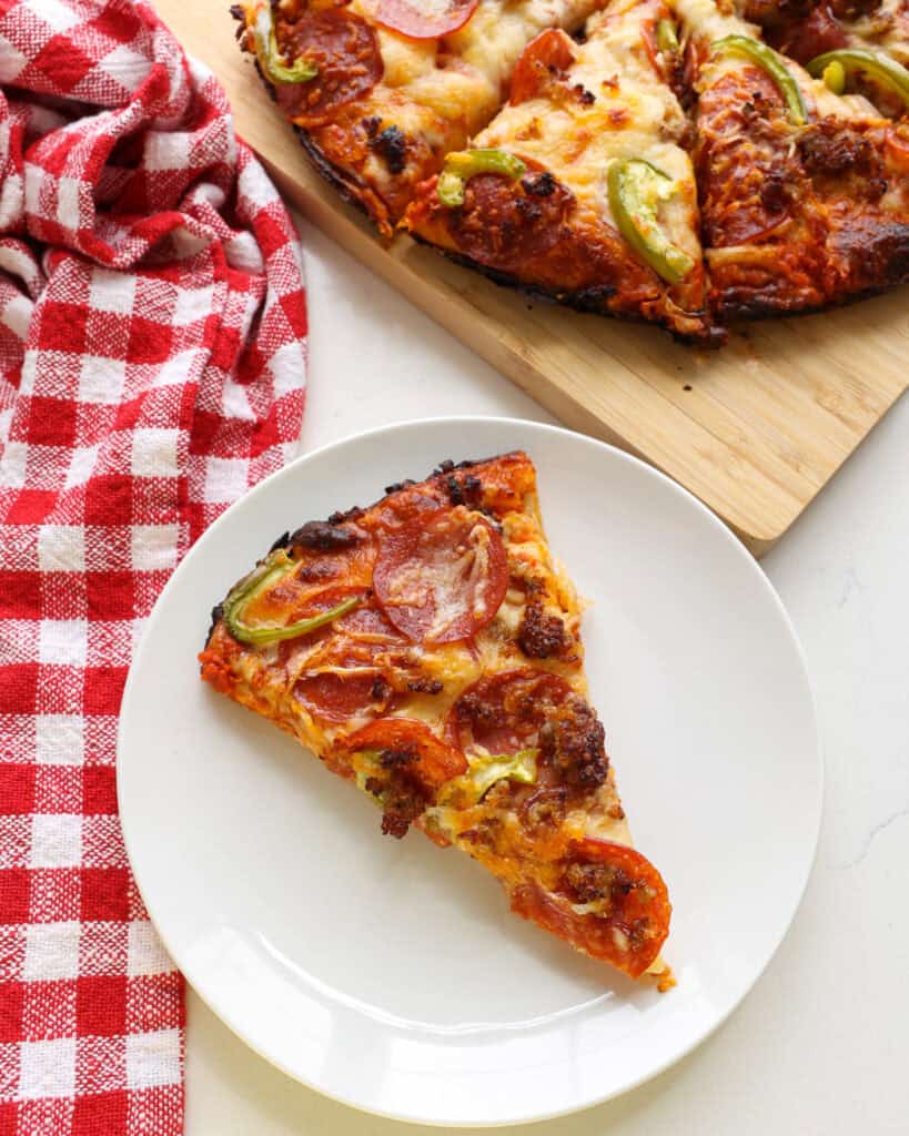 A single slice of cast iron skillet pizza on a plate in front of the rest of the pizza.