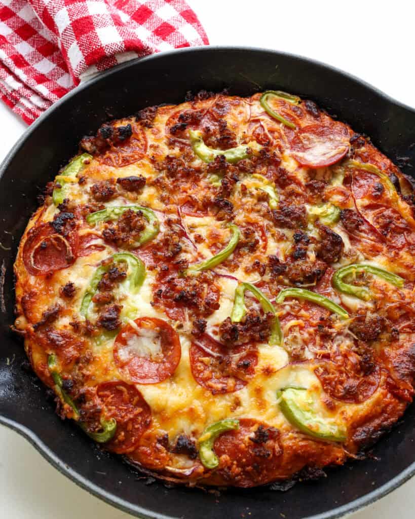 An overhead view of a pepperoni, green pepper, and onion pizza in a cast iron skillet.