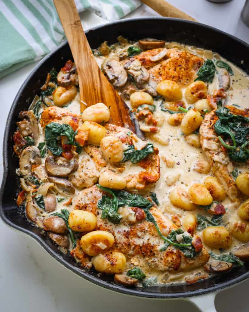 An overhead view of chicken, gnocchi, bacon, spinach, and mushrooms in cream sauce.