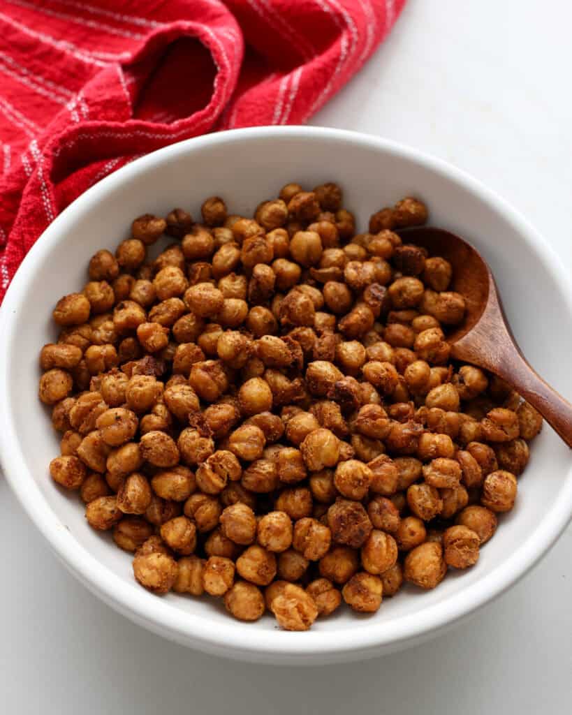 An overhead view of a white serving bowl and a wooden spoon full crispy chickpeas. 