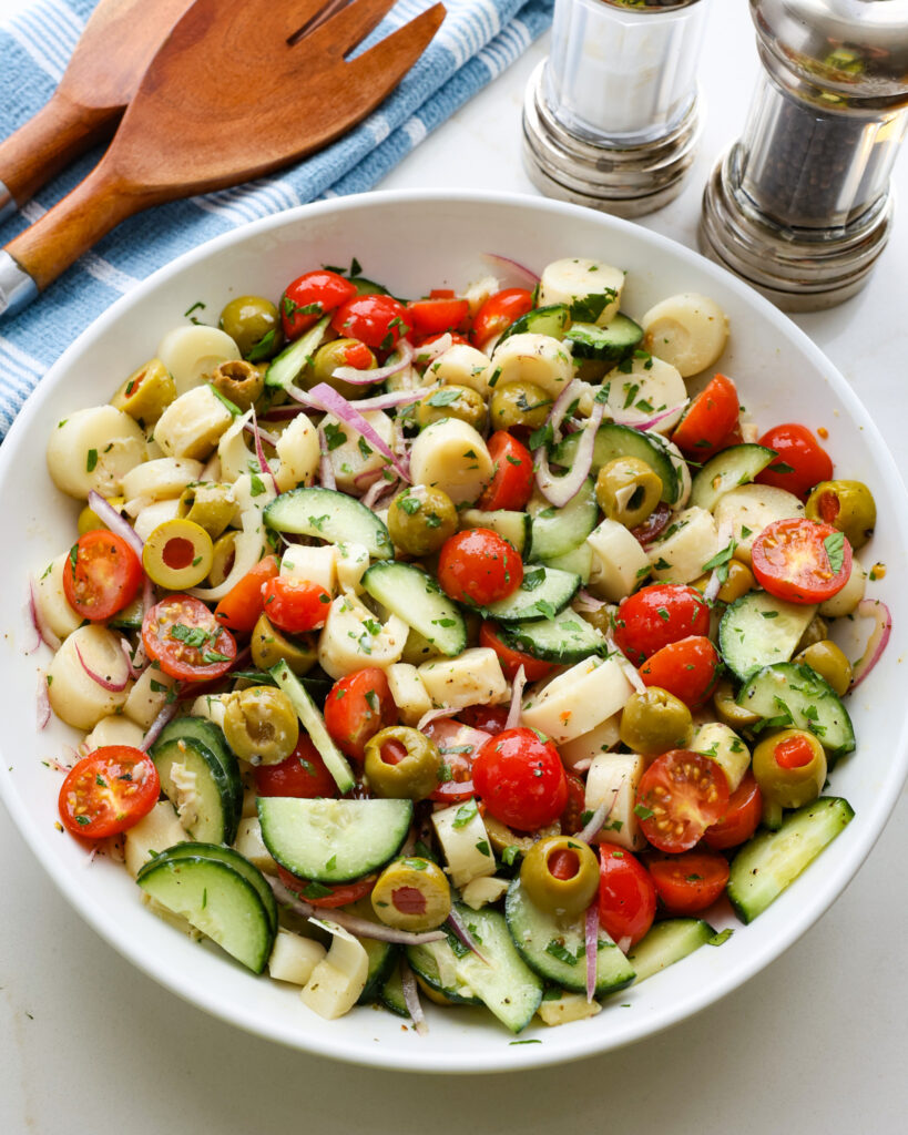 An overhead view of hearts of palm salad in a whiter serving bowl with a salt and pepper shaker and serving tongs in the background. 