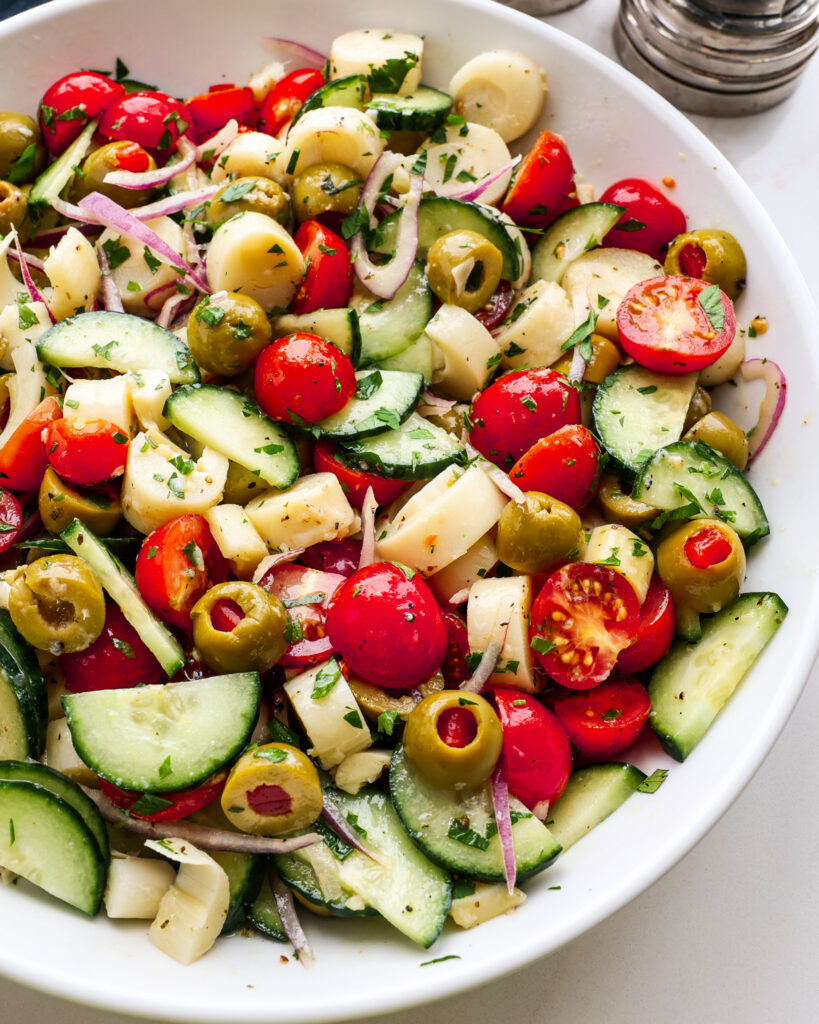 A close up view of hearts of palm salad with tender hearts of palm, red onion, cucumber, cherry tomatoes, and pimento-stuffed green olives. 