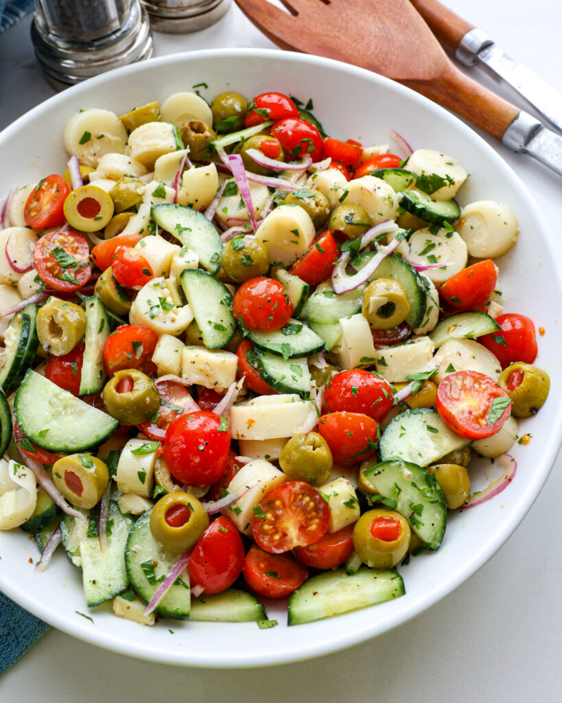 A large white serving bowl full of hearts of palm salad with salt and pepper shaker and serving pieces in the background. 