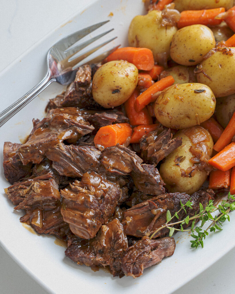 A white platter full of pot roast, poatoes, carrots, and gravy.