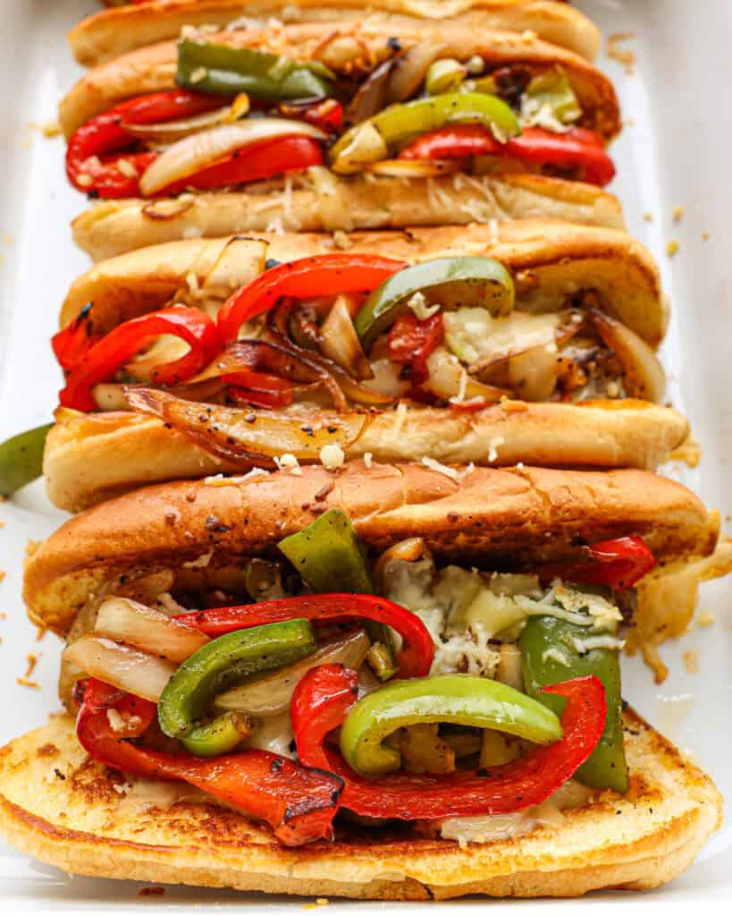 A close up view of three Italian sausage sandwiches in a white casserole dish. 