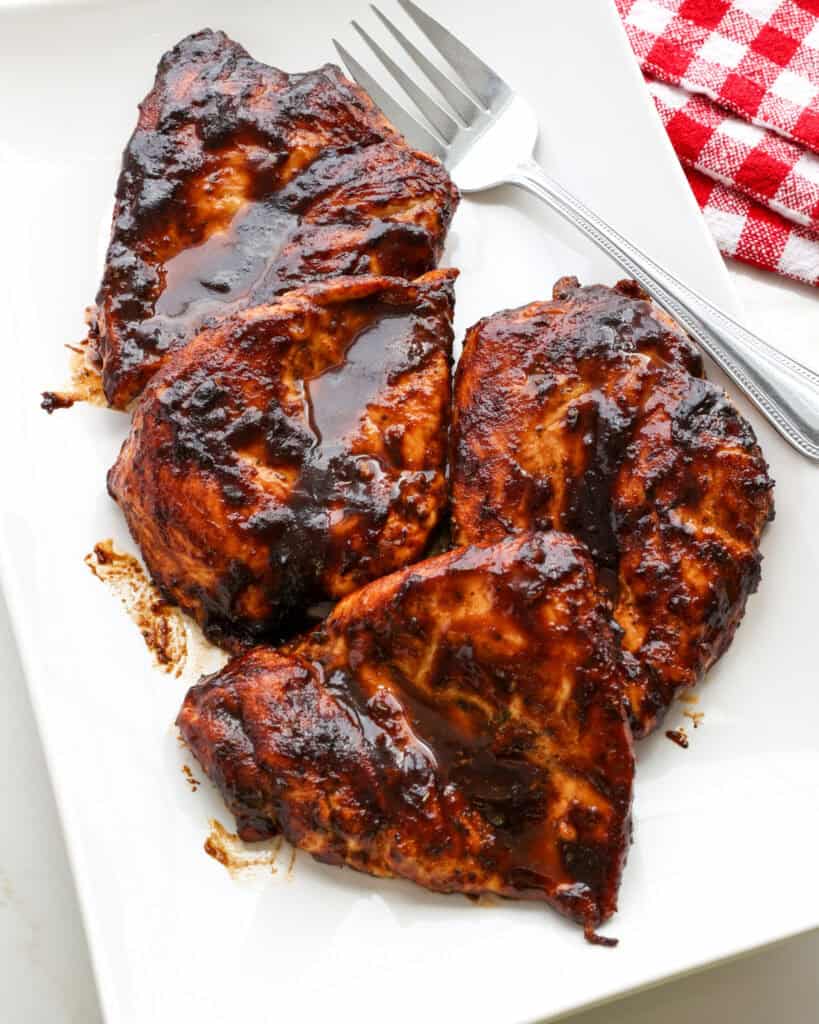 An overhead view of oven baked BBQ chicken on a white serving platter with a meat fork.