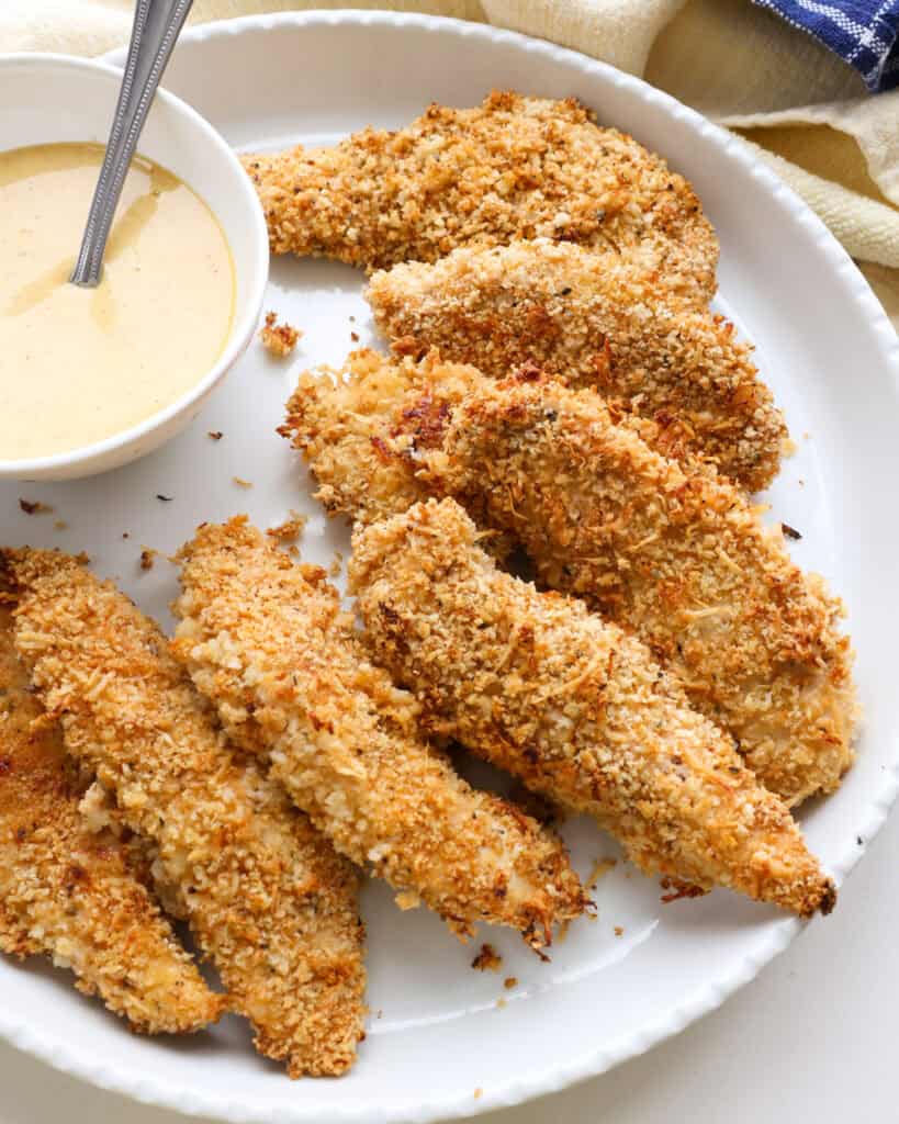 An overhead view of oven baked chicken tenders on a round white platter.