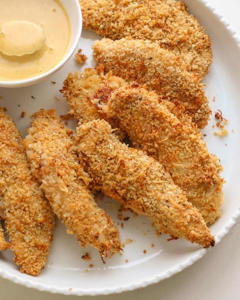 A close up view of baked chicken tenders and a bowl of honey mustard sauce.
