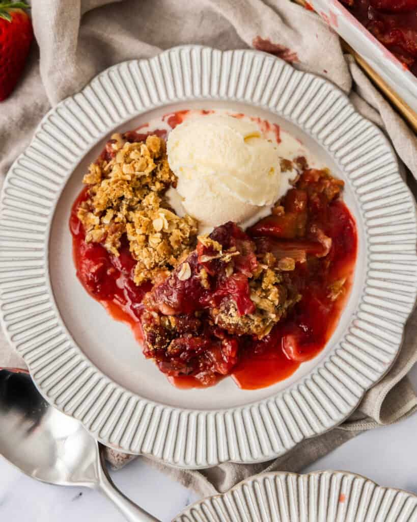 Strawberry Rhubarb Crumble Strawberry rhubarb crisp wiht a cscoop of vanilla ice cream on a white serving plate.