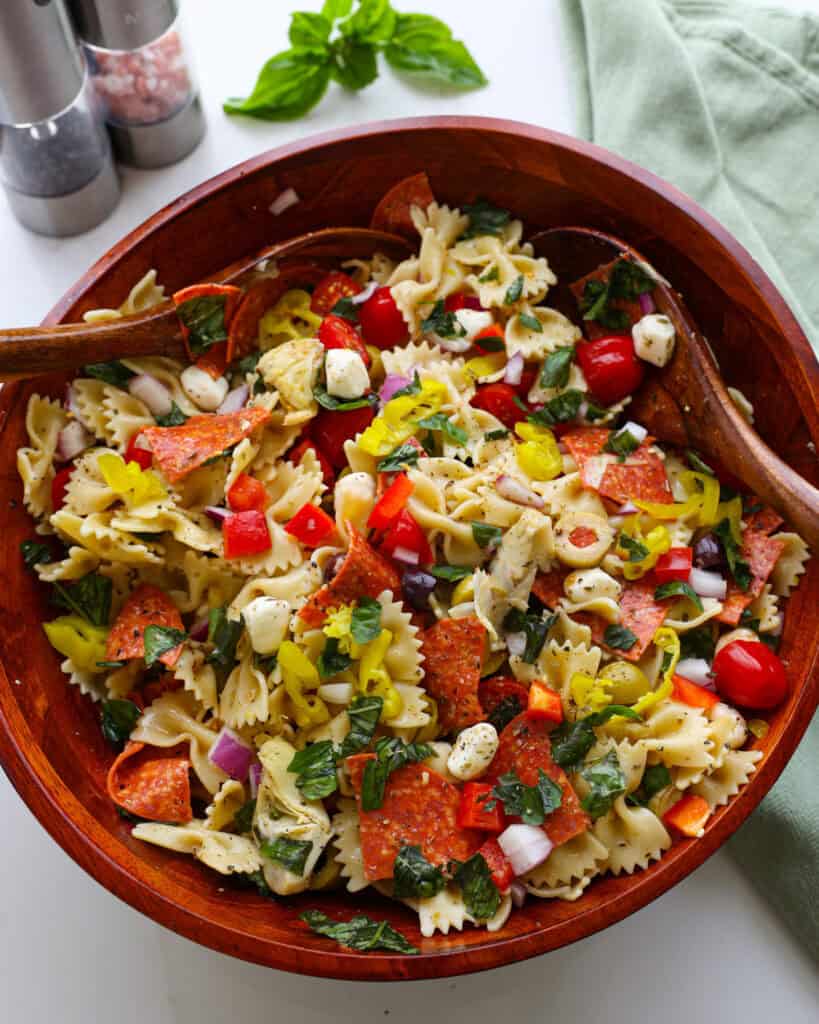 A wooden bowl and salad tossers full of antipasto pasta salad.