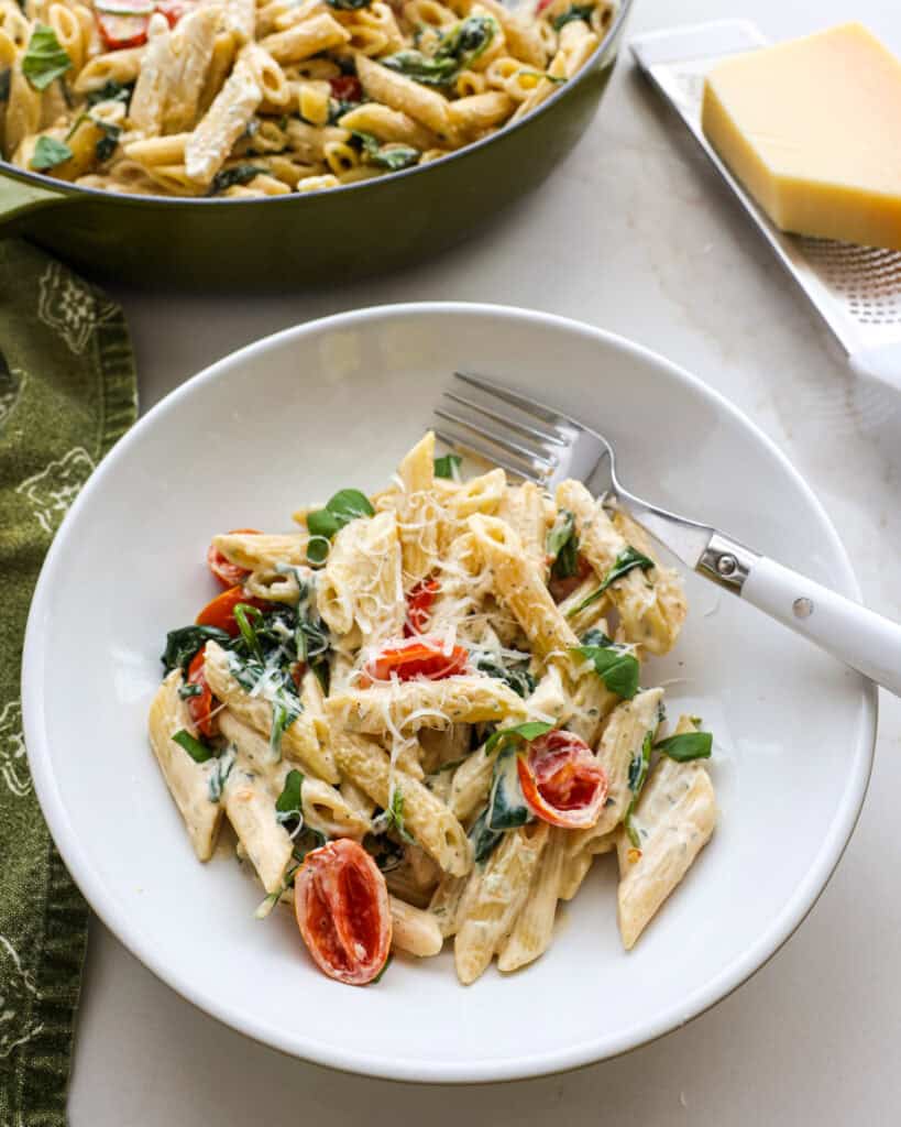 A single serving bowl full of Boursin pasta with the skillet full of pasta in the background.