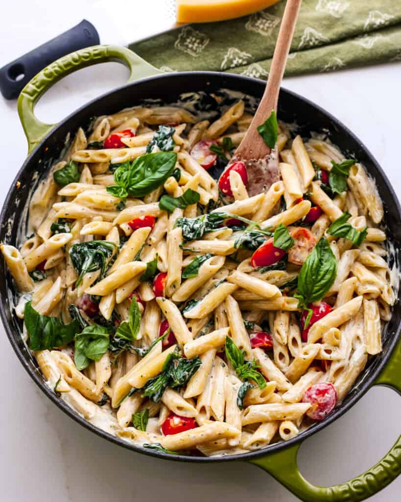 A large green skillet full of Boursin pasta with tomatoes, spinach, and fresh basil.