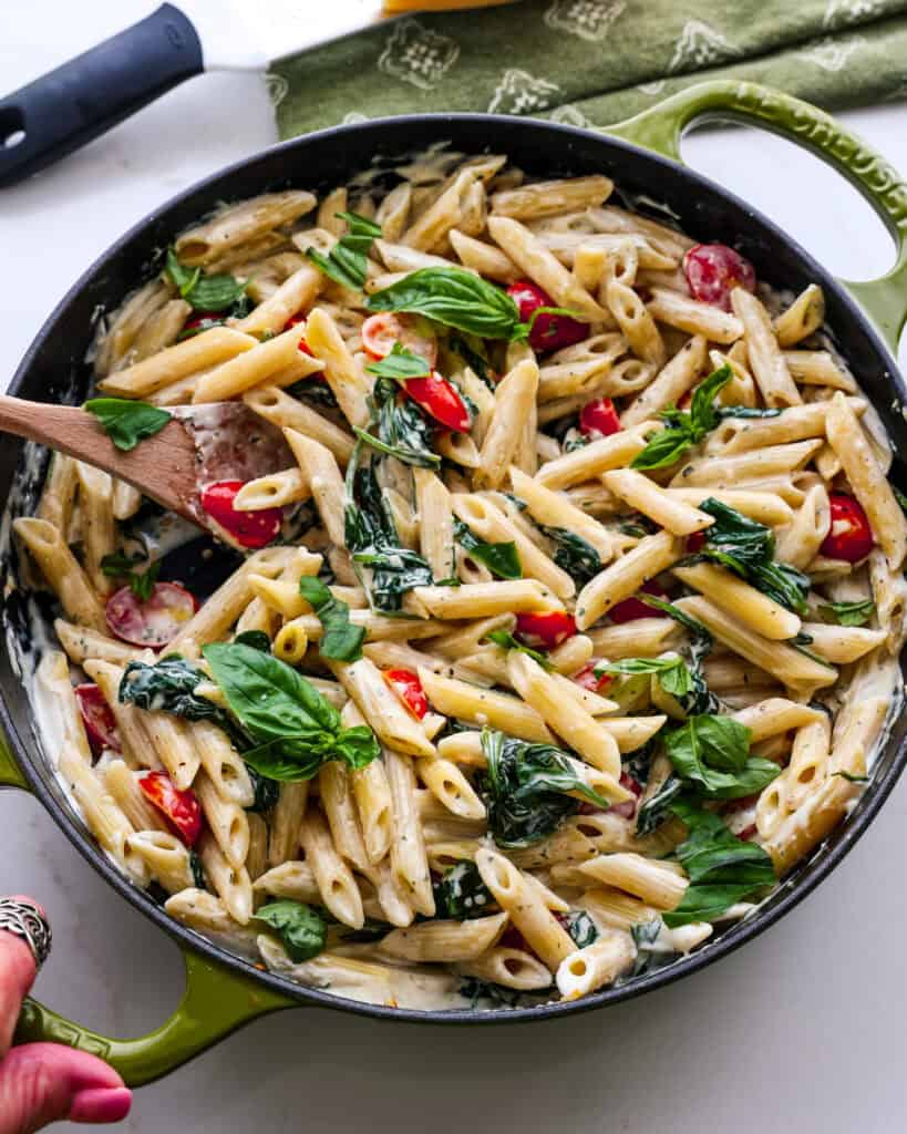 A large green skillet full of Boursin pasta witha green kitchen towel in the background.