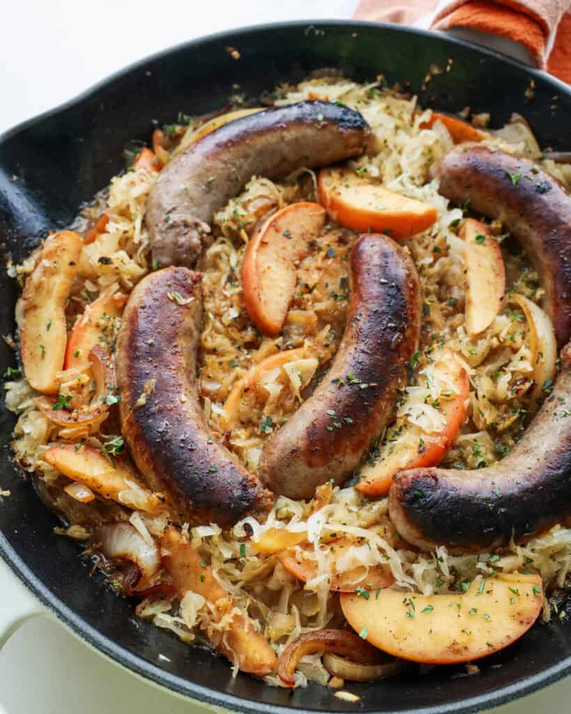 Bratwurst, sauerkraut, and apples in a large cast iron skillet. 