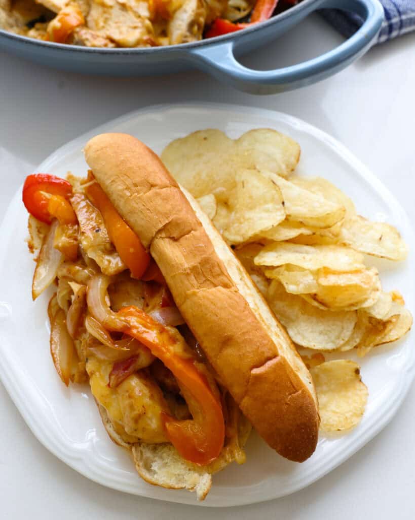Chicken cheesesteak on a white single serving plate with potato chips.