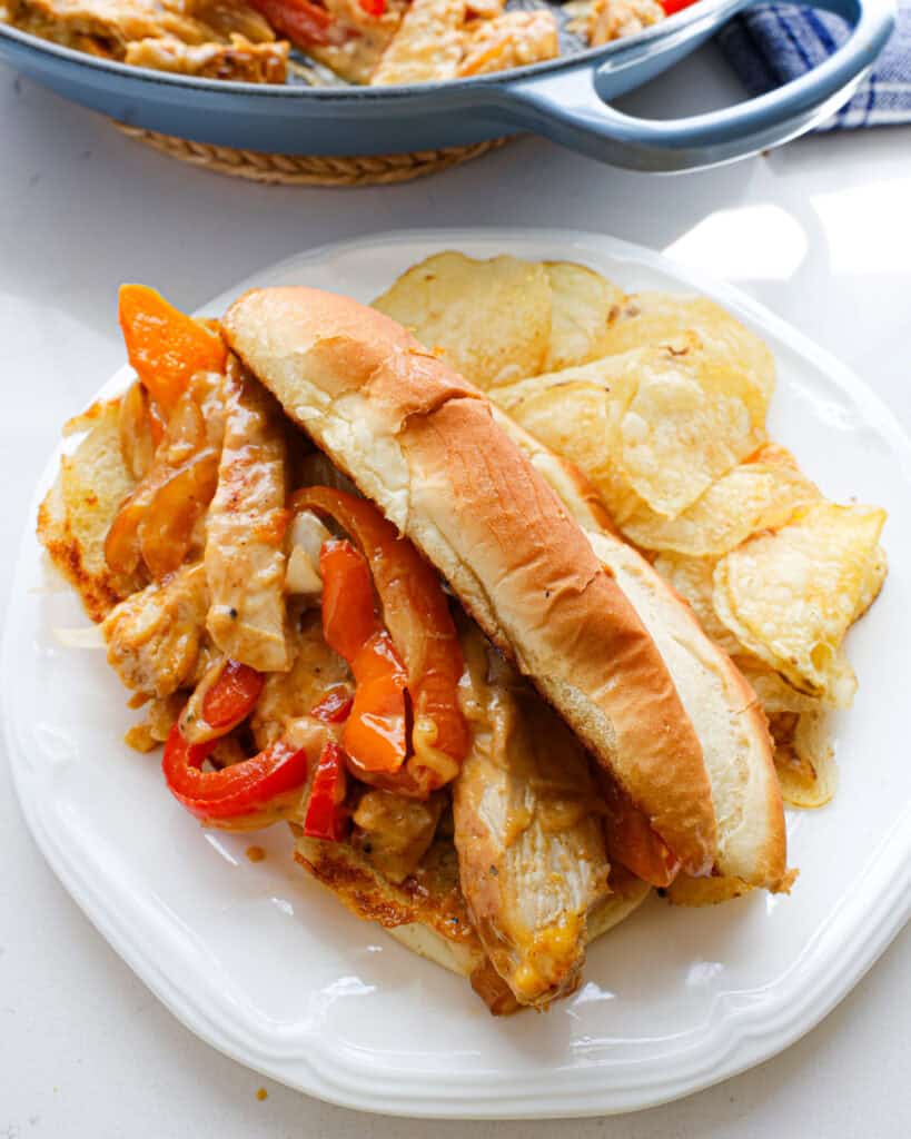 Chicken cheesesteak on a toasted bun with potato chips on the side.