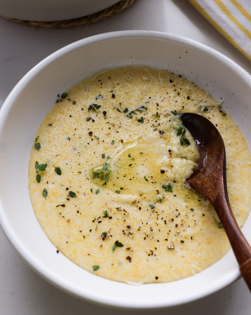 A close up view creamy polenta in a single serving bowl with a wooden spoon.