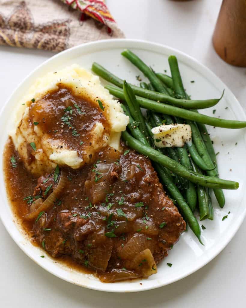 Cube steak and mashed potatoes with gravy on a plate with green beans.