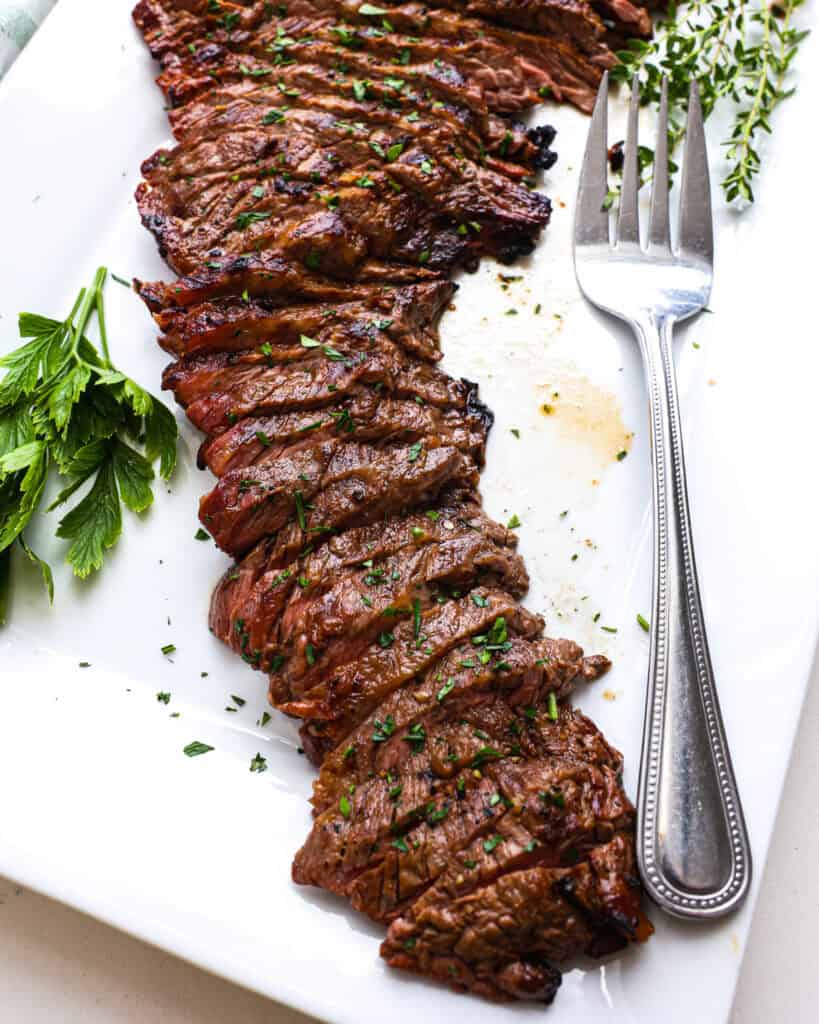 An overhead view of sliced, grilled, marinated skirt steak on a white platter. 