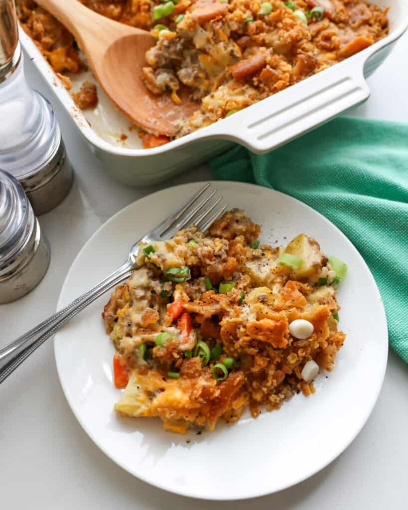 An overhead view of hobo casserole on a single serving plate with a salt and pepper shaker and the casserole dish full of it in the background. 