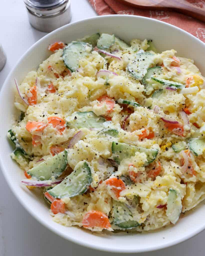 A close up view Japanese potato salad in a white serving bowl.