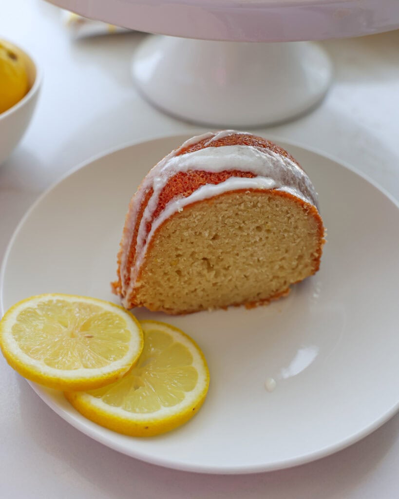 A slice of lemon bundt cake on a white plate with lemon slices. 