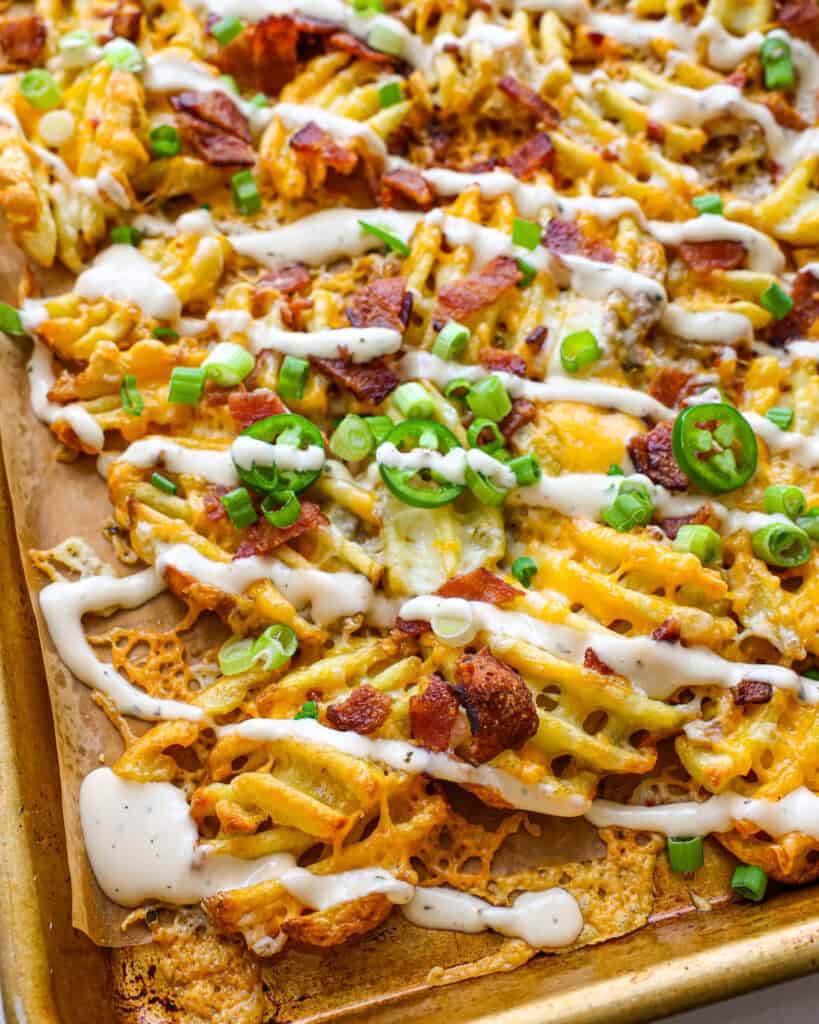 A close up view of loaded waffle fries on a large baking sheet.