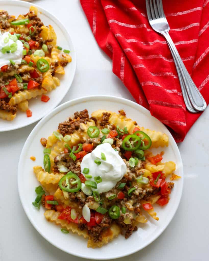 Two plates full of nacho fries topped with diced tomatoes, green onions, jalapenos, and sour cream.