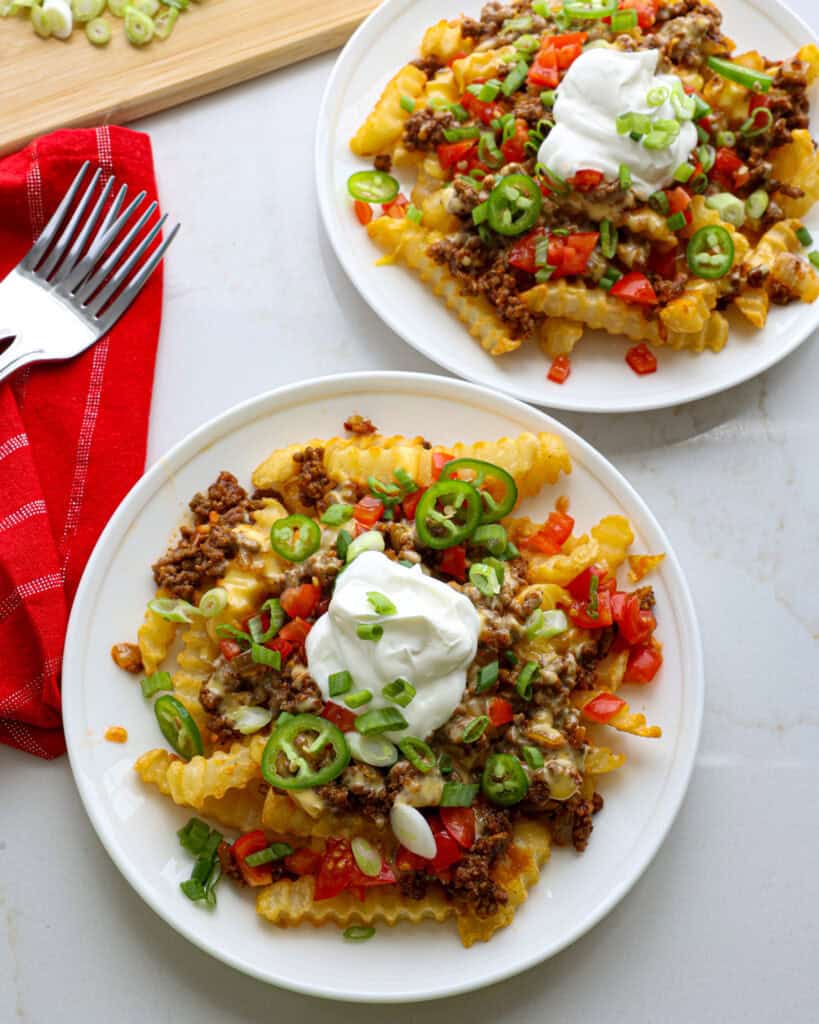 An overhead view of two plates of nacho fries with red napkins and forks in the background.