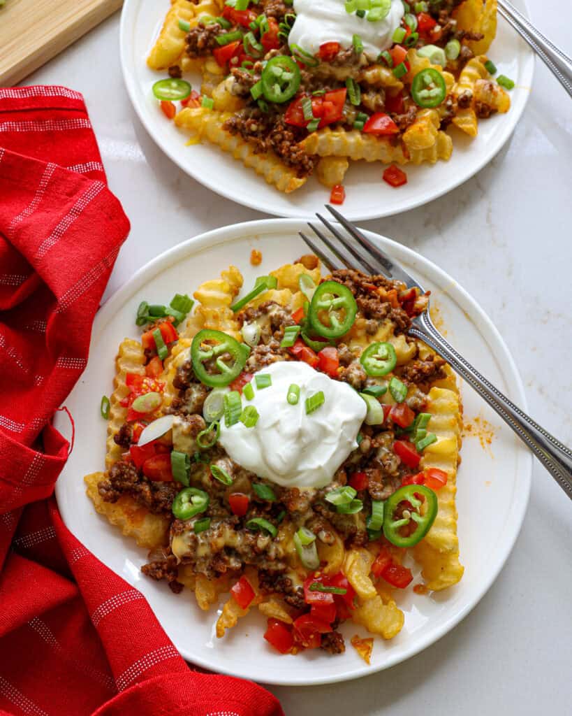 A close up view of a plate full of nacho fries with a fork on it.
