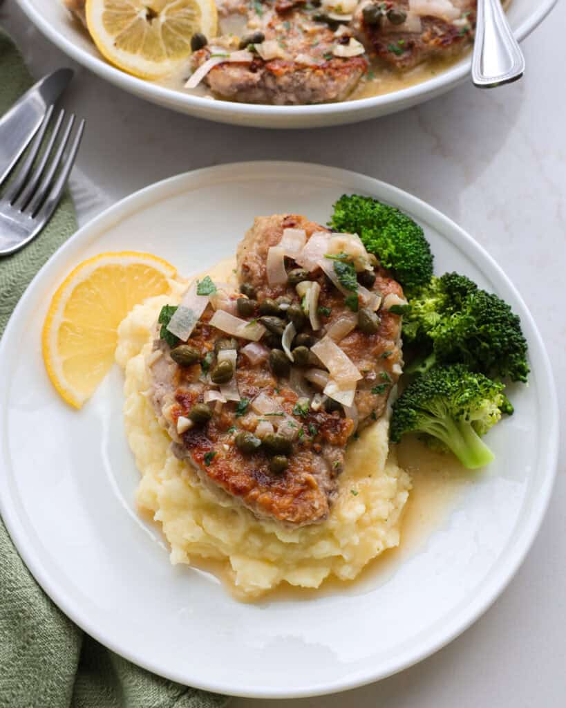 Two pieces of pork piccata drizzled with lemon butter sauce over mashed with steamed broccoli on the side.