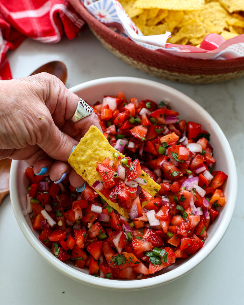 Strawberry salsa on a corn chip over a bowl full of strawberry salsa. 